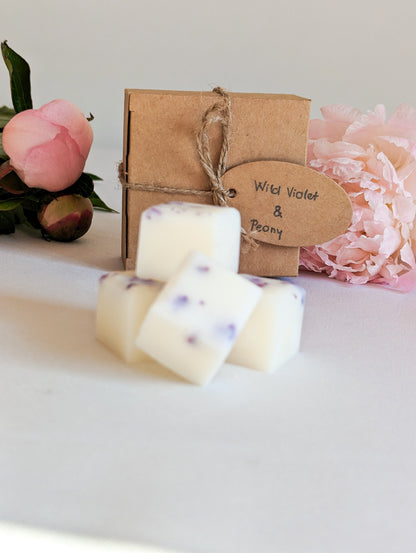 Peony wax melts with botanicals and eco friendly packaging in the background with the name of the wax melts on the tag saying wild violet & peony scented wax melts